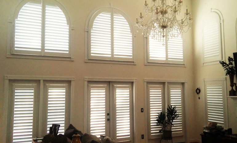 Family room in two-story Austin home with plantation shutters on high windows.