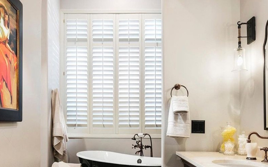 Polywood interior shutters are mold-resistant and functional within your bathroom. Photo credit: Room Resolutions White Polywood shutters above a soaking tub.